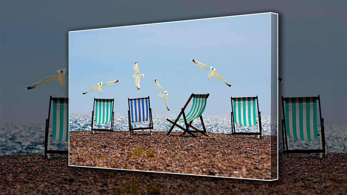 Canvas print of a pebble beach with gulls flying over beach chairs